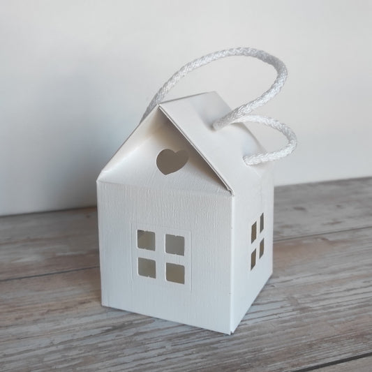 Scatola-Lanterna a forma di casetta in cartoncino fibra colore bianco. Misura 8 cm x 8 cm, H 12 cm ed è completa di manico in corda.