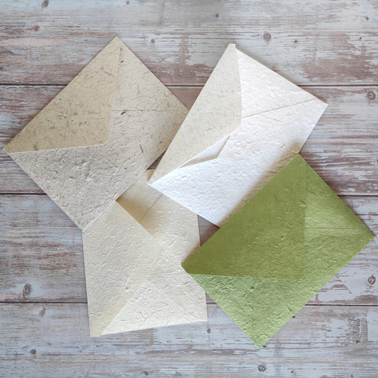 Buste formato A5 in carta di gelso artigianale, vari colori, su tavolo di legno rustico.