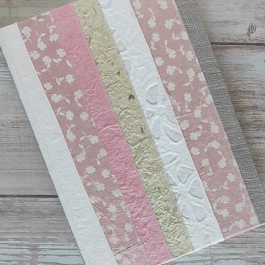 Diario rilegato con copertina rigida rivestita con un patchwork di carte artigianali cucite tra loro. Tonalità rosa, bianco e naturale.