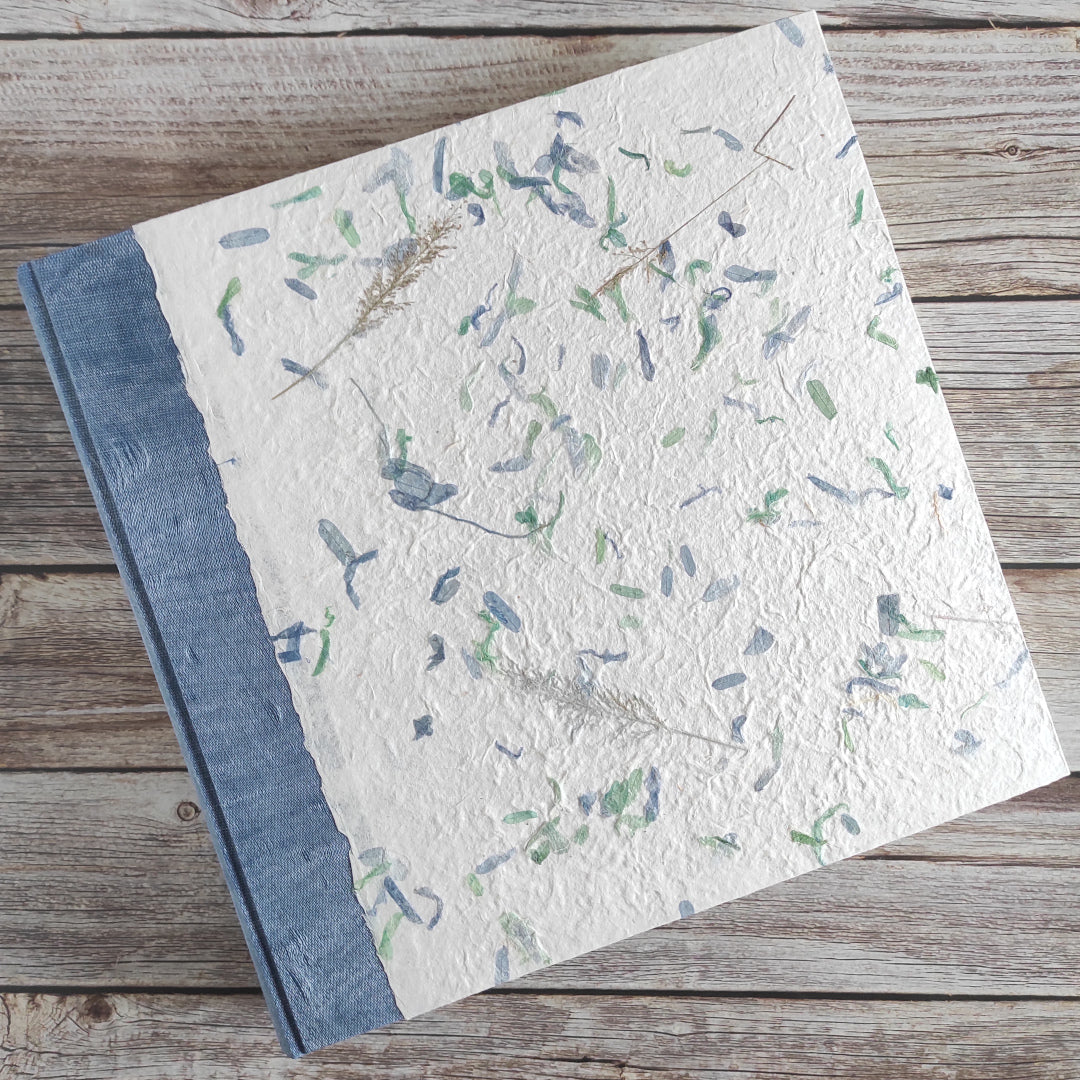 Album fotografico artigianale con copertina a due colori in carta di gelso con piccoli petali blu e verdi abbinata a carta lokta wax cotton blu